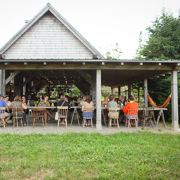 People sitting at a long table under the cover of a barn roof